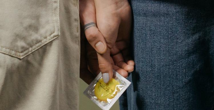 Two people holding hands and holding a condom packet.