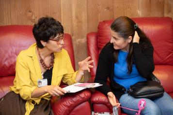 Two women sitting in red armchairs talking about information in a folder