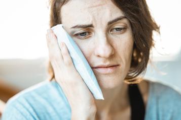 Woman holding cold compress to face with a sad facial expression