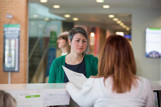 Woman talking to a receptionist about some paperwork in a hospital