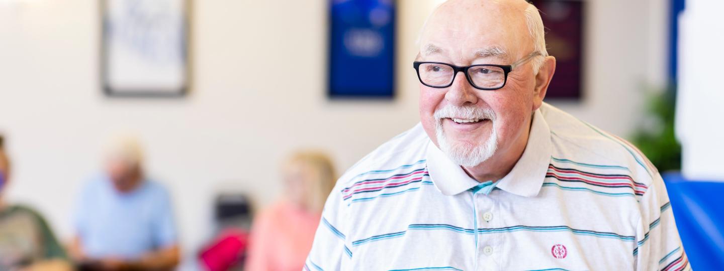 Elderly white man standing smiling in a waiting room.