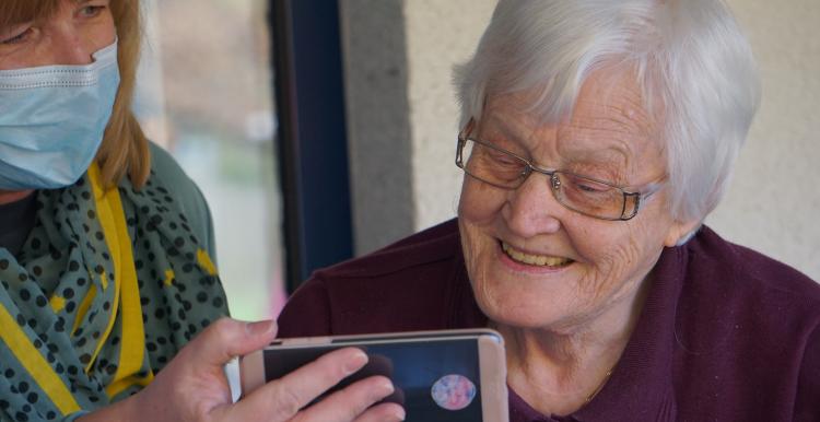 Lady in a mask showing an elderly lady her phone