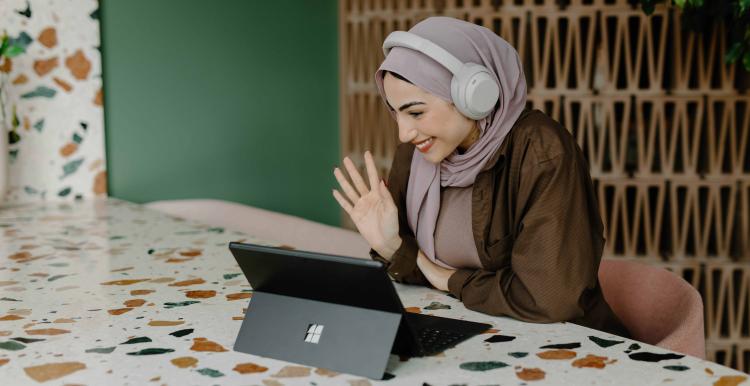 a woman sitting at a table smiling and waving at a laptop