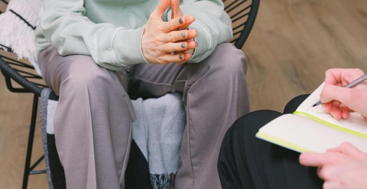 Two people sitting on chairs talking, only hands and lower bodies are visible.