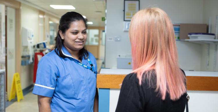 Nurse talking to a woman with pink hair in a hospital corridor