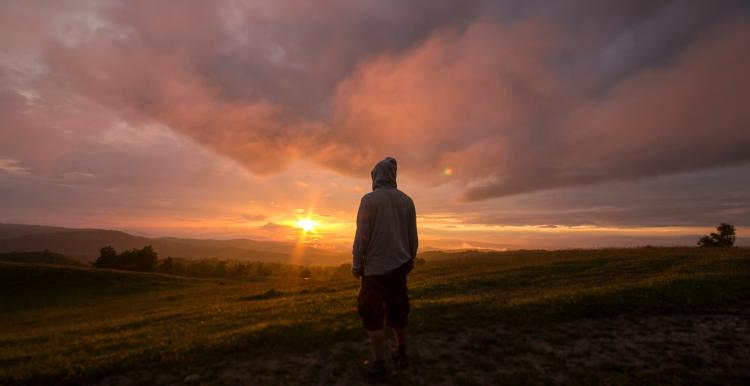 Silhouette of a man in a hooded jacket looking at a sunset