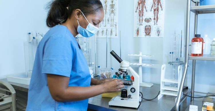 Black nurse looking at a microscope in a laboratory