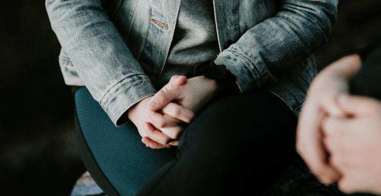 Two people sitting in a dark room talking each with their hands clasped together