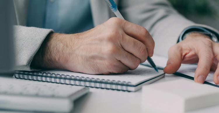 Person writing in notebook with only hands and arms visible