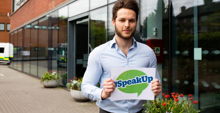 Man holding a sign outside a hospital that says 'Speak Up' 