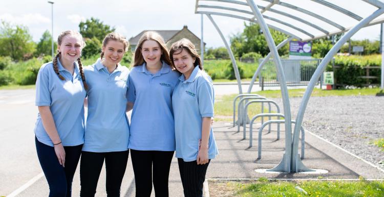 Four girls stood outside a bike shed in a line with their arms round each other