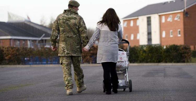 Rear view of a male soldier in uniform walking with a lady pushing a buggy