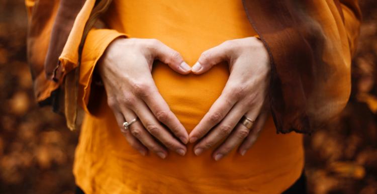 Pregnant woman in orange top with hands forming a heart