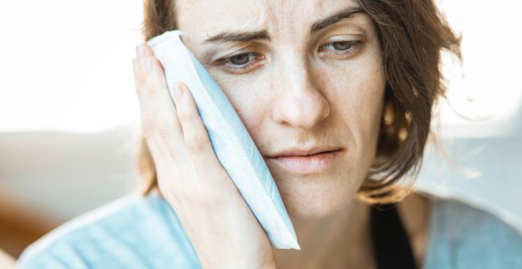 Woman holding cold compress to face with a sad facial expression