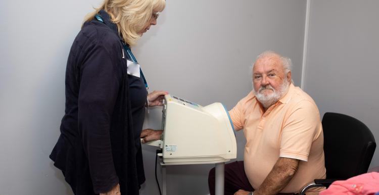 Older white man having his blood pressure checked with a lady standing alongside to help.