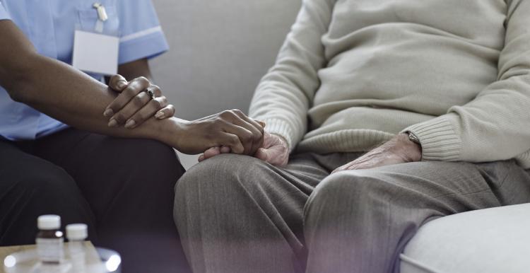 A nurse holding an old man's hand on the sofa.