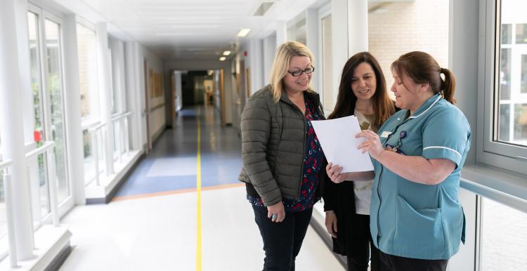 Two women talking to a nurse in a hospital corridor