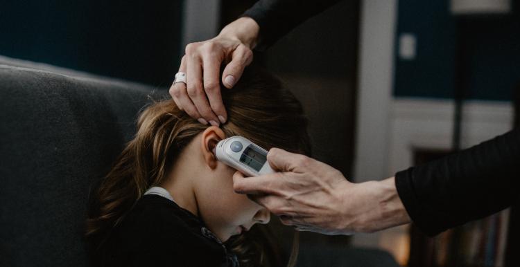 Child having temperature taken with thermometer in ear.