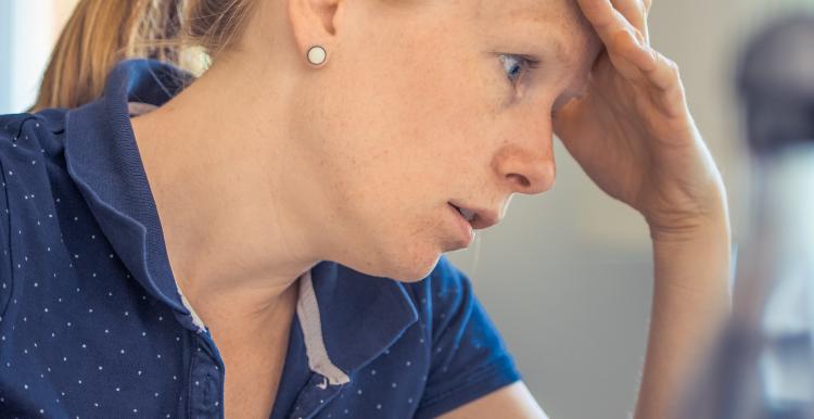 Woman sitting at a table with a laptop looking frustrated.