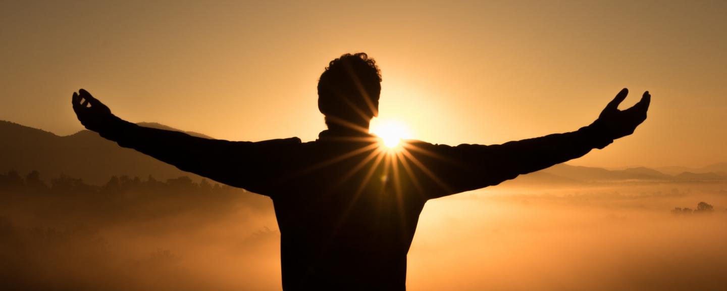 Man standing with arms outstretched looking at a sunset