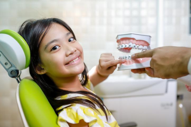 Young Asian girl in a dentist chair with her finger touching a mould of teeth and mouth