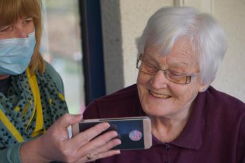 Lady in a mask showing an elderly lady her phone