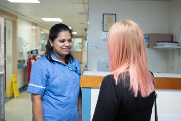 Nurse talking to a woman with pink hair in a hospital corridor