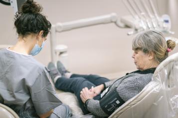 Woman sitting in a dentist's chair having her blood pressure taken by a dentist