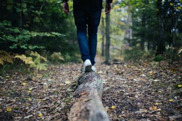 Image of person's legs as they walk and balance along a fallen tree log in the woods.