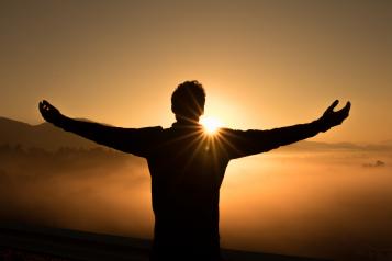 Man standing with arms outstretched looking at a sunset
