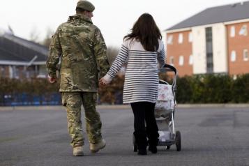 Rear view of a male soldier in uniform walking with a lady pushing a buggy