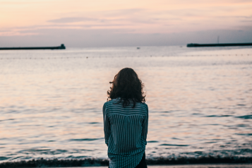 Woman with her back to camera sitting on a beach looking out to sea