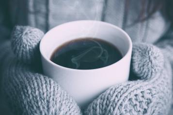 Hands wearing mittens holding a mug of hot drink