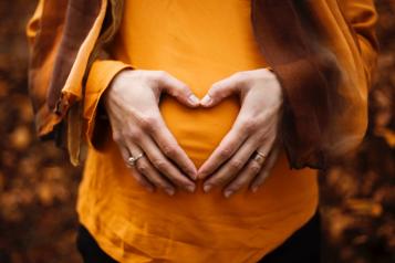 Pregnant woman in orange top with hands forming a heart