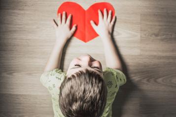 Boy with back to camera holding a red cut out heart on a table