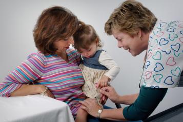 Nurse giving an infant a vaccination while parent holds the baby.