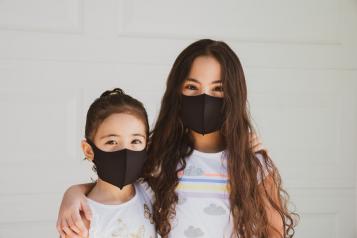 Two young children facing camera both wearing masks