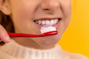 Image of smiling child with a red toothbrush holding pink toothpaste