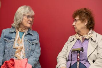 Two older ladies sitting and talking with a red background behind
