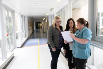 Two women talking to a nurse in a hospital corridor