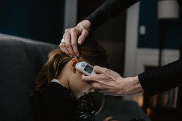 Child having temperature taken with thermometer in ear.