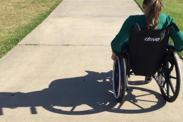 A woman in a wheelchair outside on a path.
