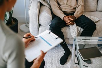 Person taking notes while speaking to somebody seated on a sofa