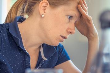 Woman sitting at a table with a laptop looking frustrated.