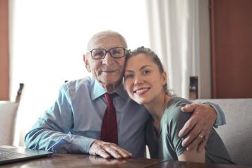 Elderly man hugging a young lady while sitting at a table.