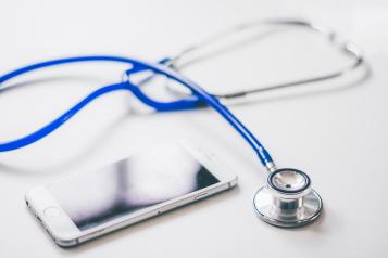 blue stethoscope and grey mobile phone on white background