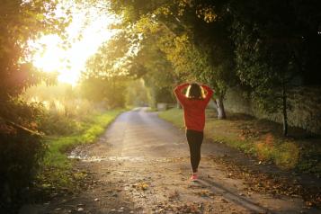 Girl wearing a red jumper walking down a leafy lane with arms outstretched