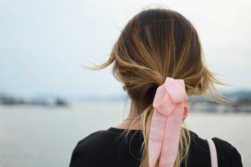 Reverse headshot image of a woman with long hair tied back with a pink ribbon