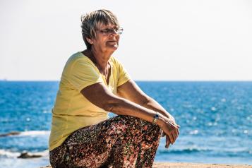 Older white woman sitting on rocks at the beach looking out to sea