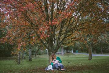 Woman sitting under a tree feeding a baby